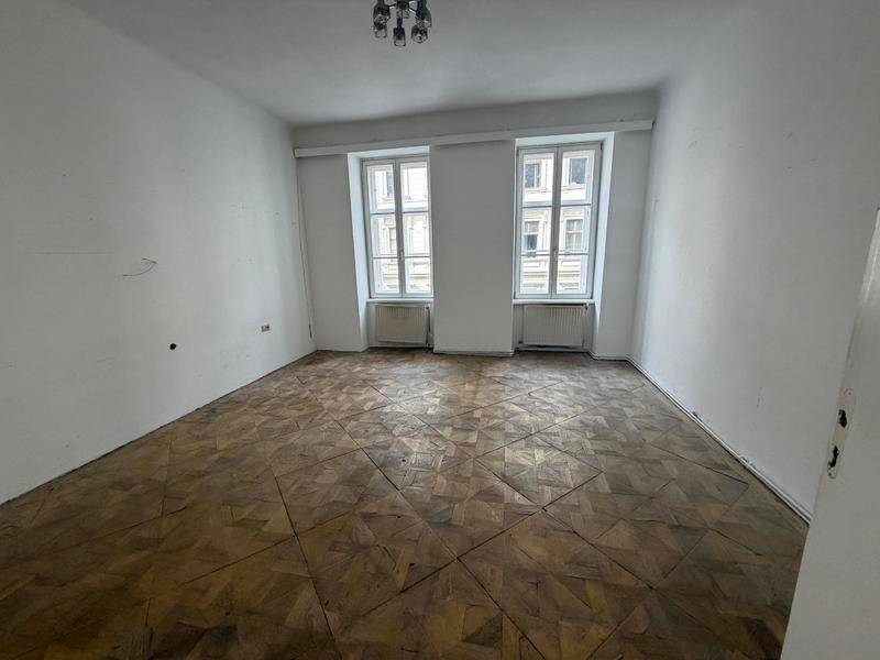 Geräumiges Zimmer mit gemustertem Parkettboden und zwei großen Fenstern.