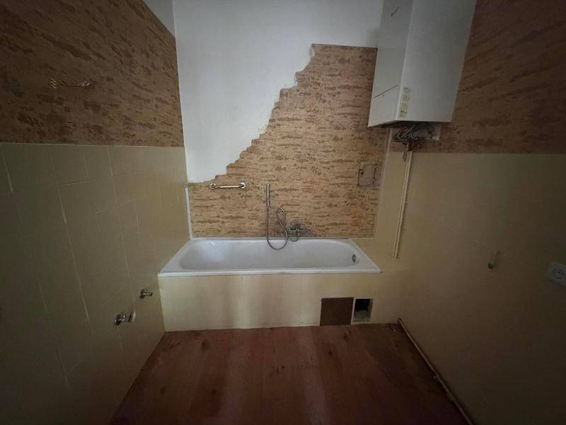 Badezimmer in Renovierung mit Badewanne, Wandfliesen und Warmwasserbereiter.