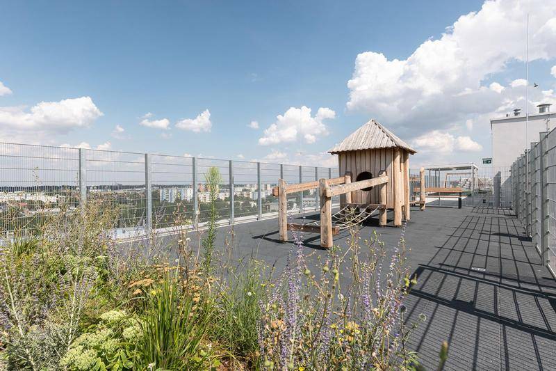 Dachspielplatz mit Holzspielhaus, weichem Bodenbelag und weitem Blick über die Stadt.