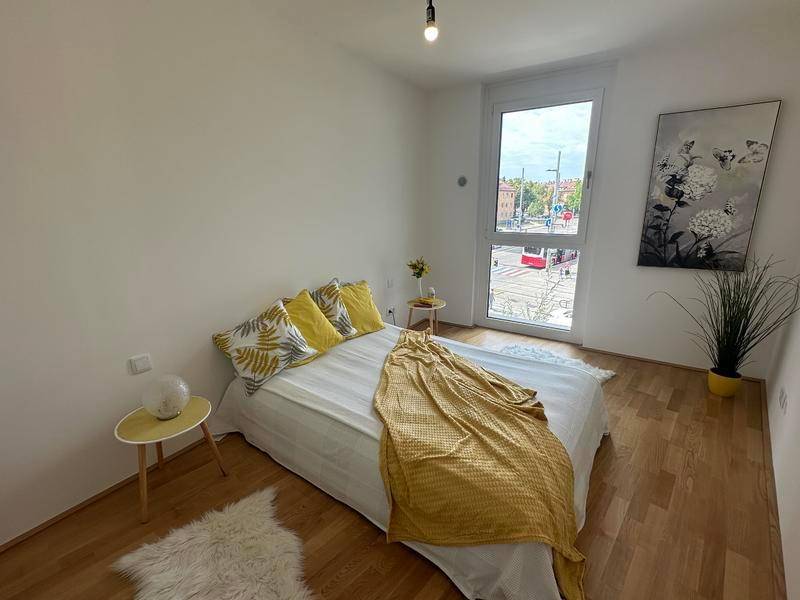Helles Schlafzimmer mit Holzboden, großem Fenster und Blick auf die Straße.