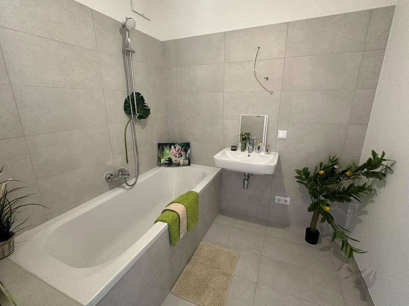 Modernes Badezimmer mit Badewanne, Fliesenboden und Waschbecken, in hellen Grautönen gehalten.
