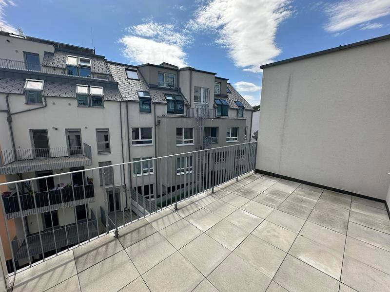 Heller Balkon mit Fliesenboden und Metallgeländer, umgeben von modernen Wohngebäuden.