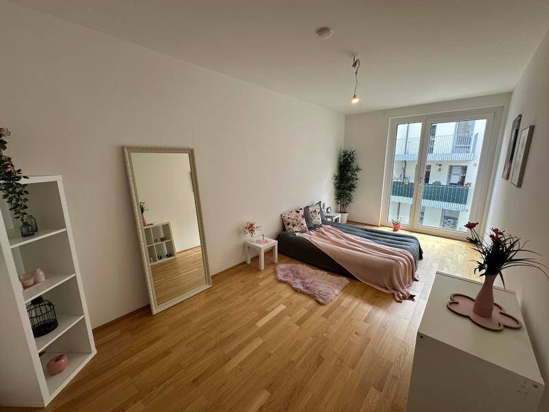 Helles Schlafzimmer mit Holzboden, großem Spiegel und Zugang zu einem Außenbereich.