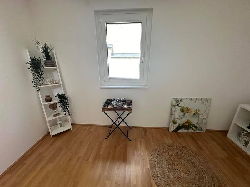 Helles Zimmer mit Holzboden, einem Fenster und einfacher, moderner Dekoration.