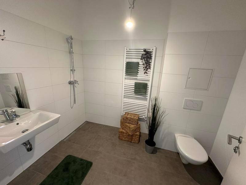 Modernes Badezimmer mit ebenerdiger Dusche, WC, Waschbecken und weißen Fliesen.