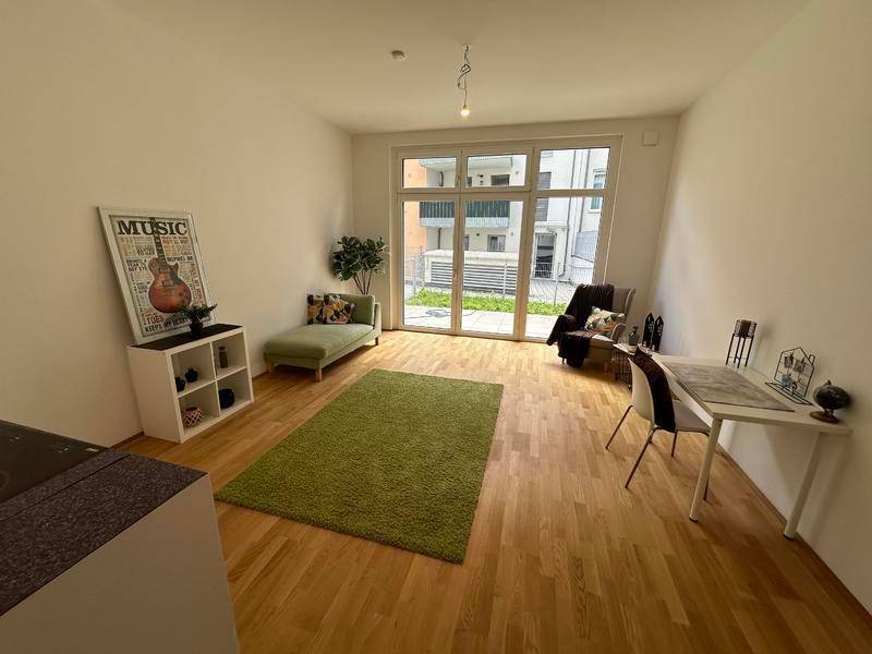 Geräumiges Wohnzimmer mit Holzboden, großem Fenster und Zugang zur Terrasse.