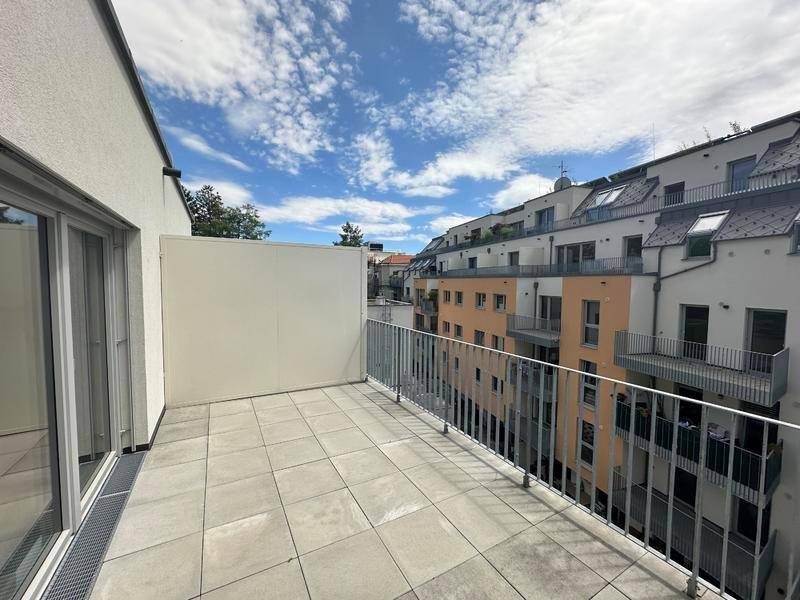 Sonniger Balkon mit Fliesenboden und Blick auf die Nachbargebäude unter blauem Himmel.