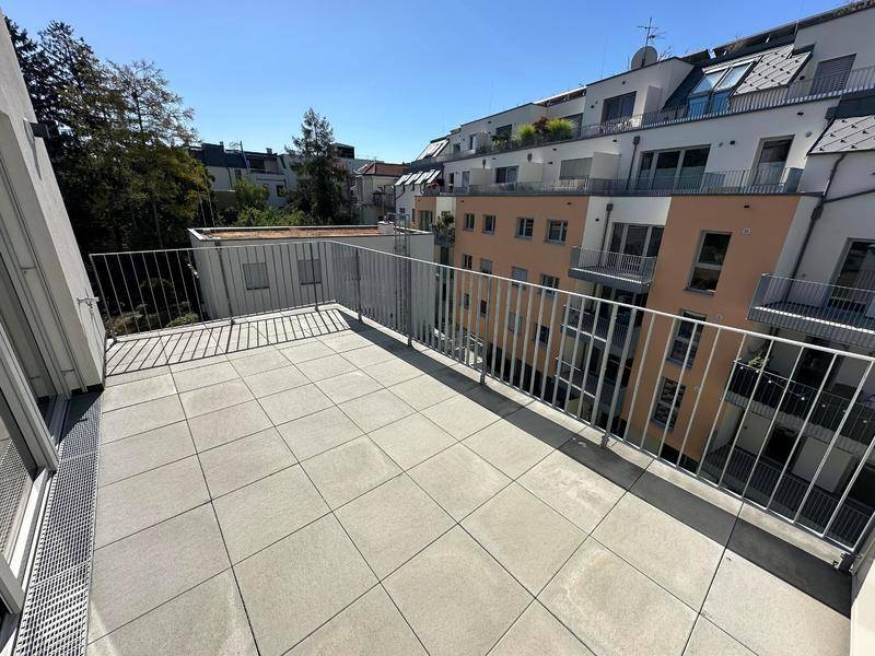 Geräumige Terrasse mit Fliesenboden und Metallgeländer, bietet einen Blick auf die umliegenden Gebäude.