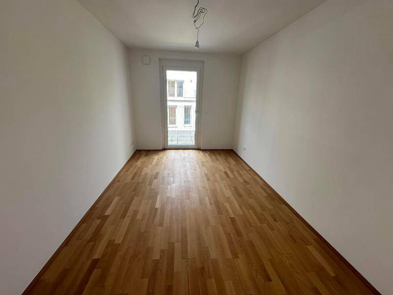 Helles Zimmer mit Parkettboden und einer Tür, die zu einem französischen Balkon führt.