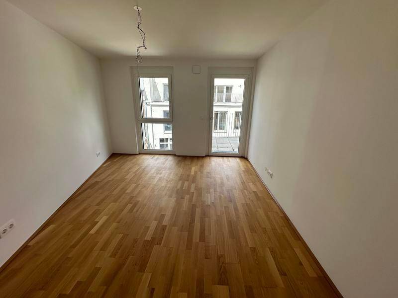 Leeres Schlafzimmer mit Holzparkett und zwei Fenstern, die viel Licht hereinlassen.