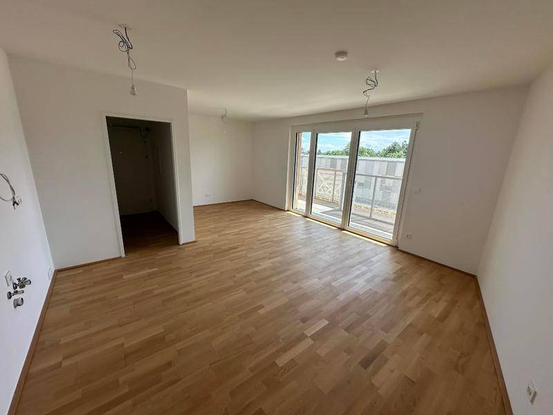 Lichtdurchfluteter Raum mit hellem Parkettboden und breiter Fensterfront zum Balkon.
