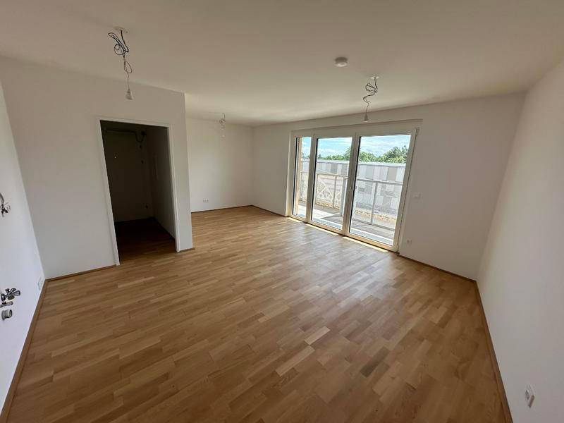 Helles, leeres Zimmer mit Parkettboden und Zugang zu einem Balkon.