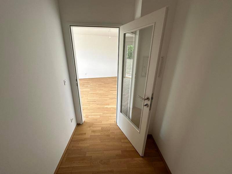 Heller Flur mit Holzboden und einer modernen Tür, die in einen weiteren Raum führt.
