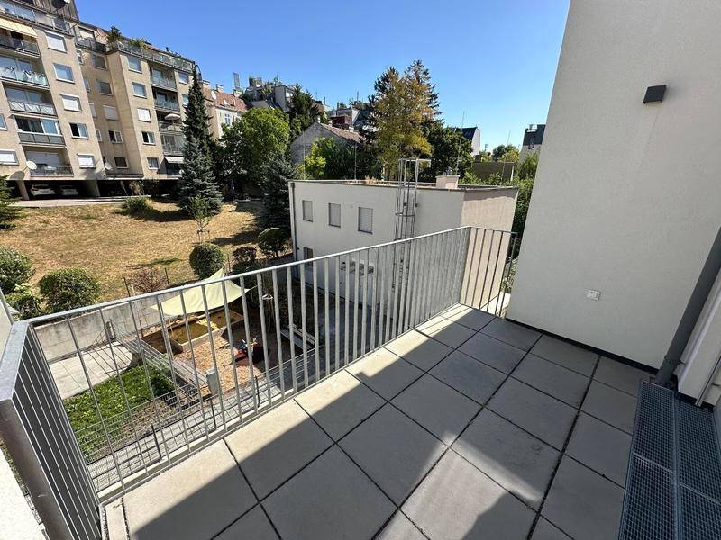 Balkon mit Fliesenboden und Blick auf einen begrünten Innenhof mit Spielbereich.