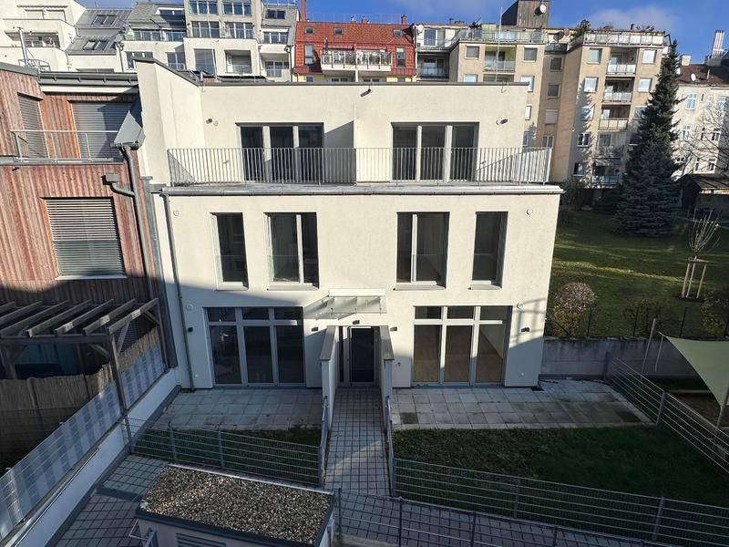 Rückansicht eines modernen Wohngebäudes mit Terrassen und kleinen Gartenbereichen.