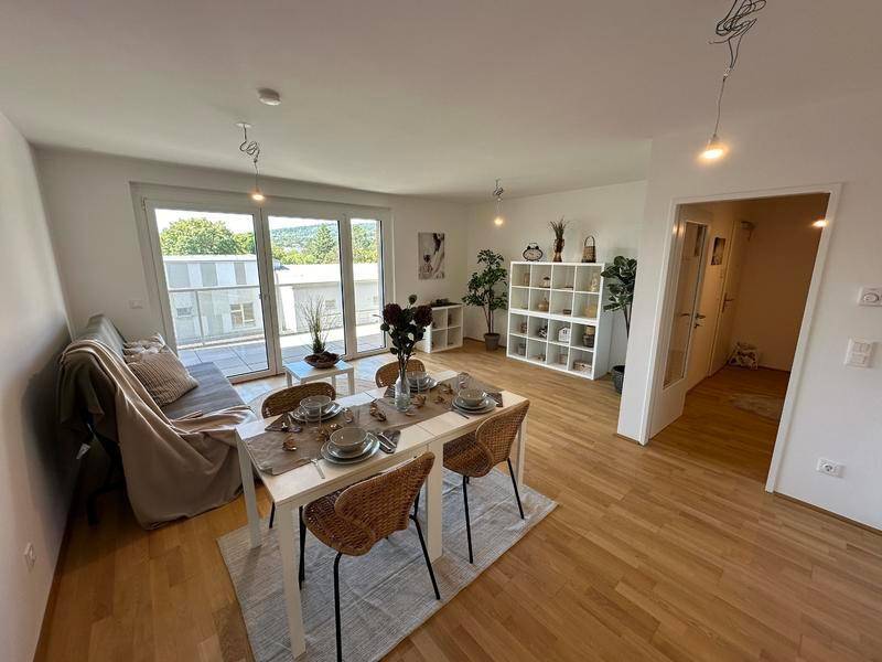 Heller Wohn- und Essbereich mit Holzboden, Zugang zum Balkon und moderner Einrichtung.