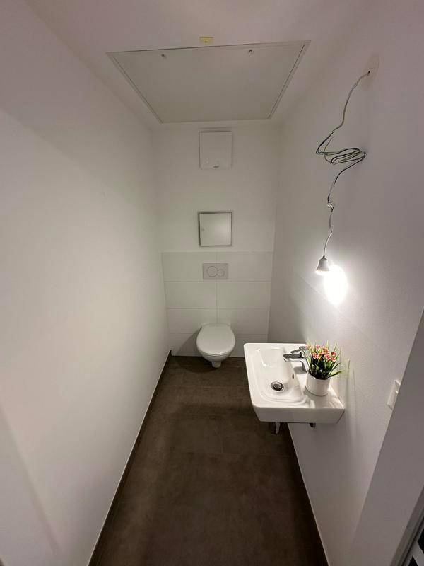 Separates Gäste-WC mit Toilette, kleinem Waschbecken und dunklem Fliesenboden.