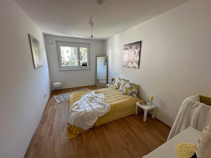 Gemütliches Schlafzimmer mit gelbem Bett, Holzboden und Fenster für natürliches Licht.