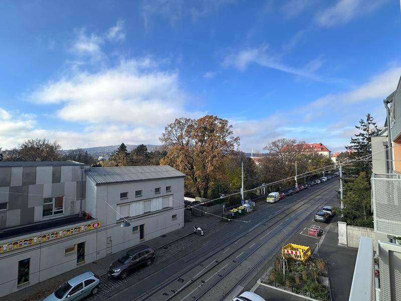 Blick von oben auf eine belebte Straße mit Straßenbahnschienen und umliegenden Gebäuden.