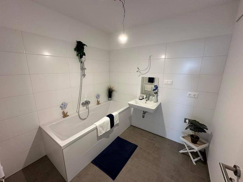 Modernes Badezimmer mit Badewanne, Waschbecken und weißen Fliesen an den Wänden.