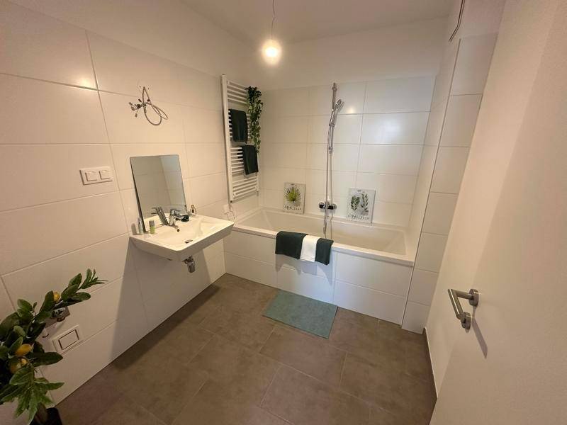 Modernes Badezimmer mit Badewanne, Wandfliesen und beheiztem Handtuchhalter, hell und sauber.