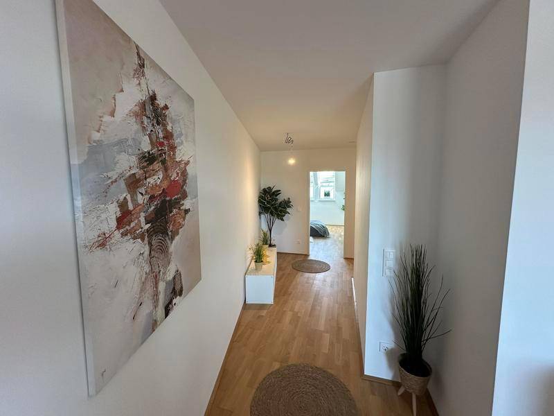 Heller Flur mit Holzboden und moderner Kunst an der Wand, führt zu weiteren Räumen.