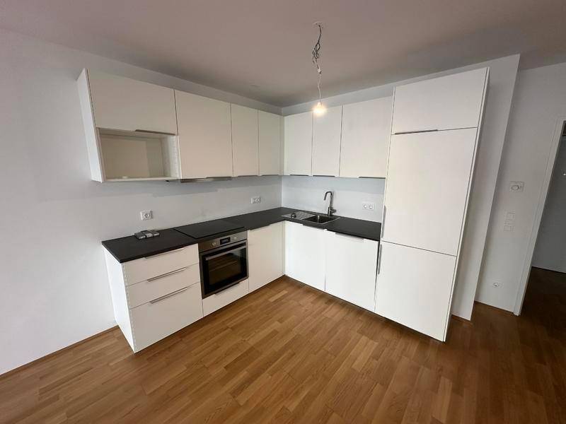 Moderne Küchenzeile mit weißen Schränken, dunkler Arbeitsplatte und integriertem Backofen.
