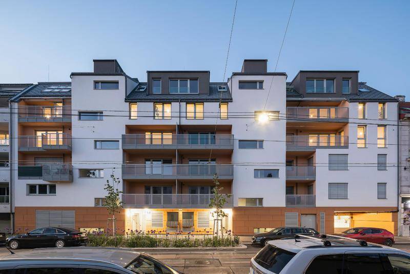 Abendansicht der modernen Wohnanlage von der Straße aus mit beleuchteten Balkonen.