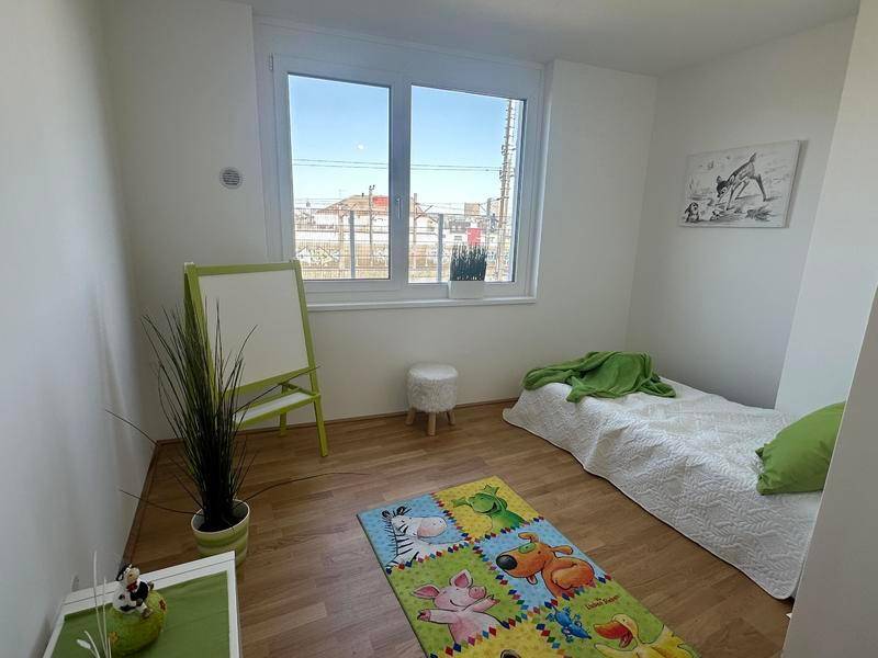 Helles Zimmer mit Holzboden, großem Fenster und bunter Spielmatte.