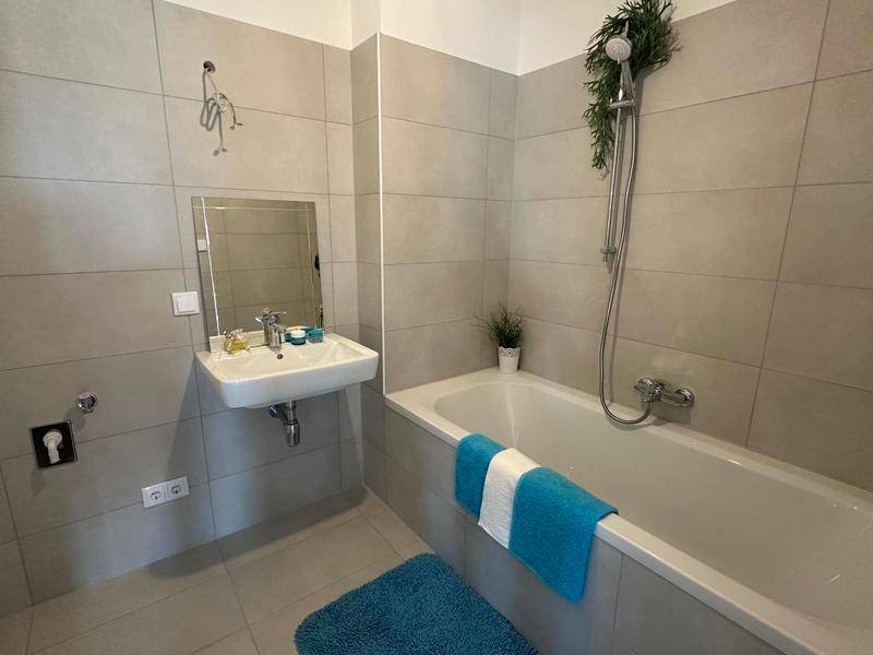 Modernes Badezimmer mit grauen Fliesen, Badewanne und Waschbecken.