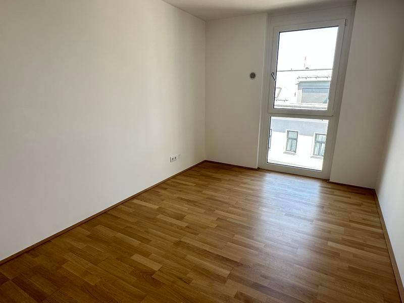 Leeres Zimmer mit Holzboden und großem Fenster, bereit zur individuellen Gestaltung.
