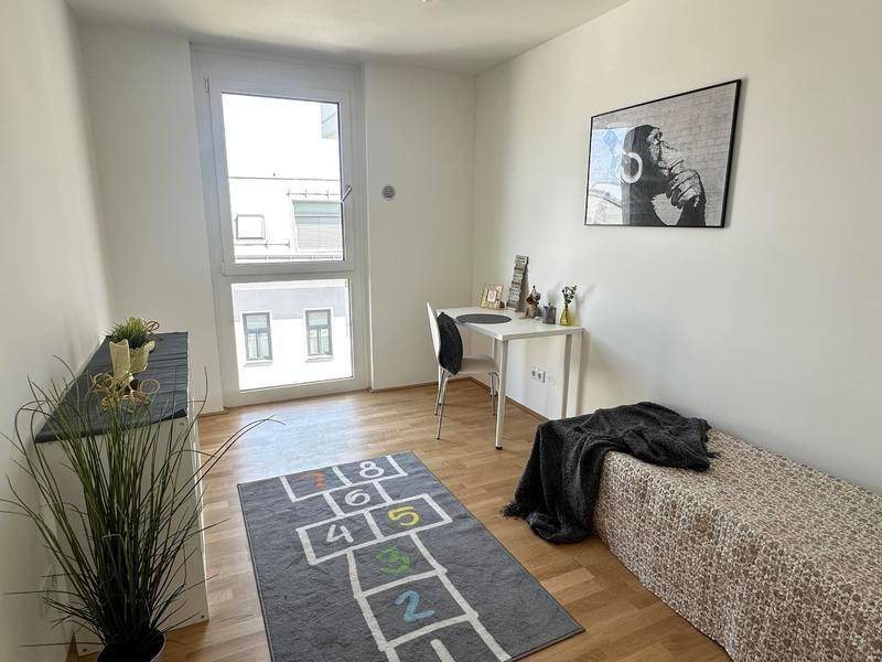 Helles Zimmer mit Holzboden, großem Fenster und einem Schreibtisch, ideal als Kinder- oder Arbeitszimmer.