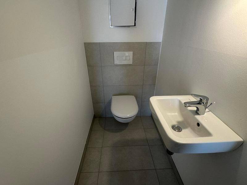 Separates Gäste-WC mit Wand-WC und kleinem Waschbecken, modern gefliest.