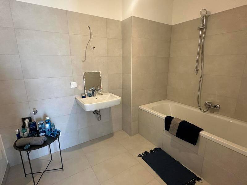 Modernes Badezimmer mit hellen Fliesen, Badewanne und Einzelwaschbecken.