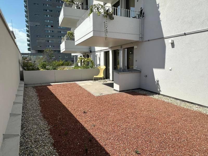 Weitläufige Terrasse mit Kiesbeet und Blick auf die moderne Wohnanlage.