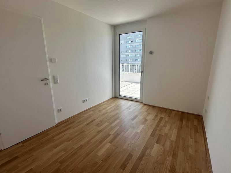 Helles Schlafzimmer mit Holzboden und Zugang zu einem kleinen Balkon, bietet Blick auf andere Gebäude.