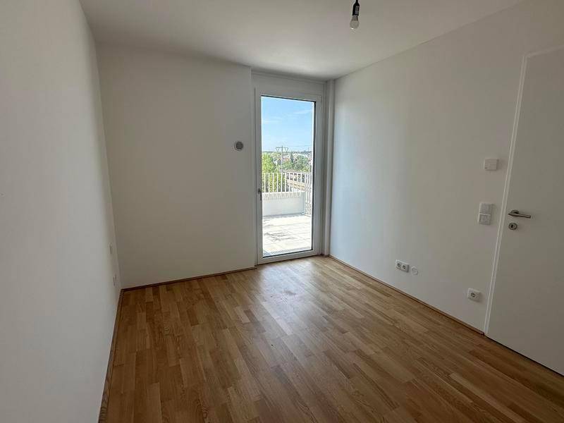 Helles Zimmer mit Parkettboden und Zugang zu einem Außenbereich.