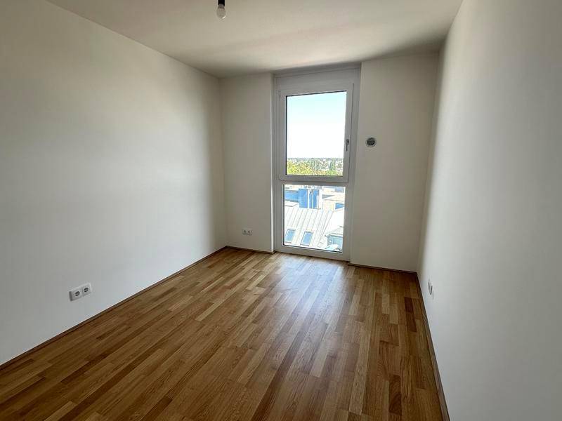 Helles Schlafzimmer mit Parkettboden und großem Fenster, das viel Tageslicht hereinlässt.