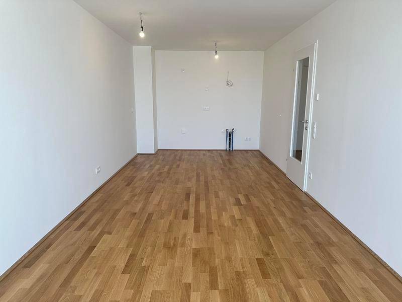 Geräumiger, unmöblierter Raum mit hellem Holzboden und weißen Wänden, bereit zur Einrichtung.
