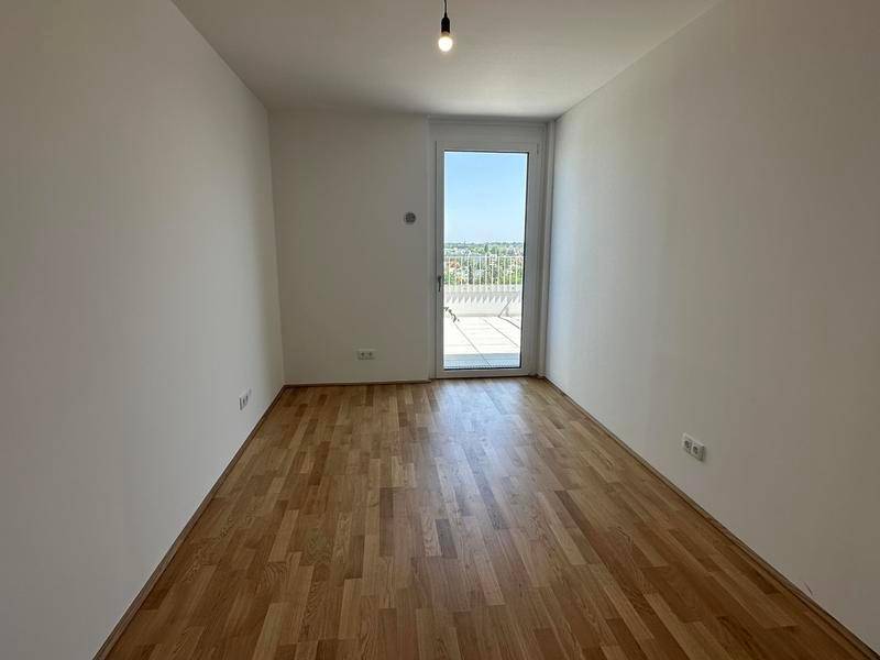 Helles Zimmer mit Holzboden und Zugang zu einem Außenbereich, ideal als Schlaf- oder Arbeitszimmer.