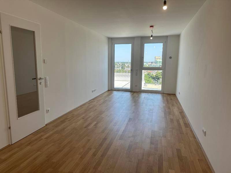 Heller, leerer Raum mit Holzboden und großen Glastüren, die auf eine Terrasse führen.
