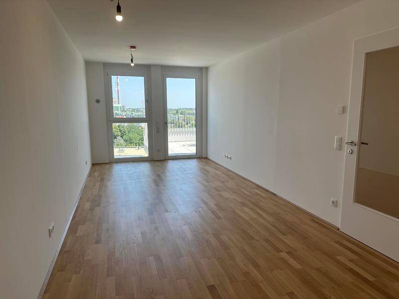 Heller, leerer Raum mit Parkettboden und Zugang zu einem Außenbereich.