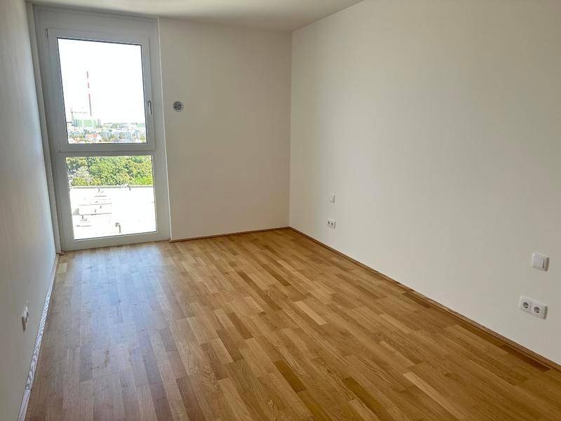 Helles Schlafzimmer mit Parkettboden und großem Fenster, das viel Tageslicht hereinlässt.