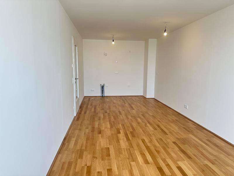 Leerer Raum mit Parkettboden und Anschlüssen für eine zukünftige Küche.