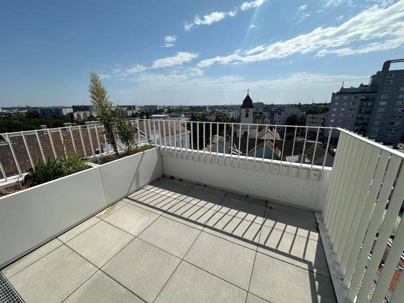 Sonniger Balkon mit Fliesenboden und Blick auf die Stadt und eine Kirche.