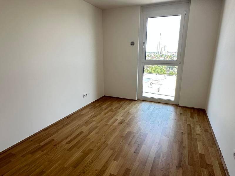 Kleines, helles Zimmer mit Holzboden und Fenster mit Blick auf die Umgebung.