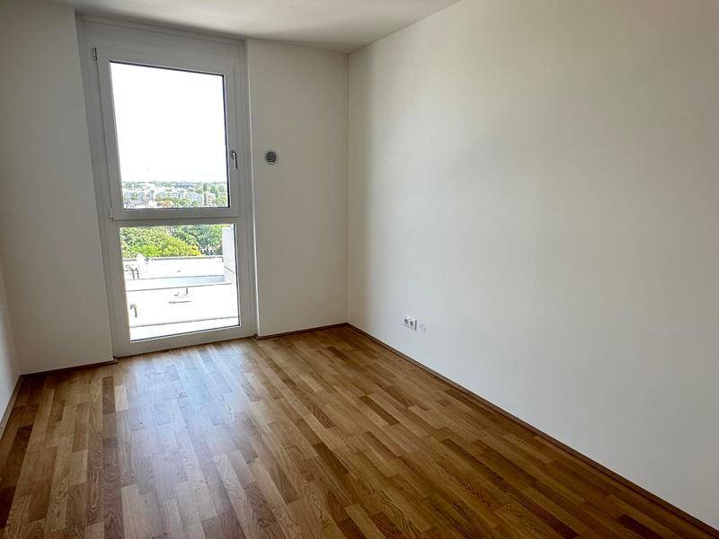 Freundliches Zimmer mit Holzboden und großem Fenster, das viel Licht spendet.