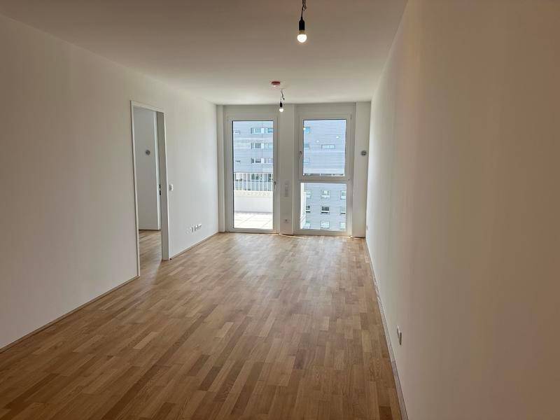 Heller, leerer Wohnraum mit Holzboden und Zugang zu einem Balkon, bereit zur Gestaltung.
