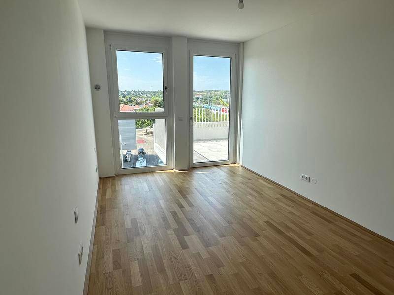 Helles Zimmer mit Holzboden und großem Fenster mit Blick ins Grüne.