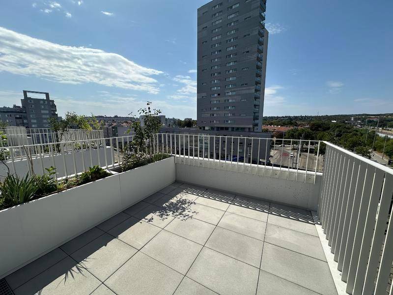 Geräumiger Balkon mit Fliesenboden und Blick auf die Stadt und ein Hochhaus.